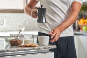 Egy férfi kávét tölt kávéfőzőből egy pultra helyezett kerámia csészébe.