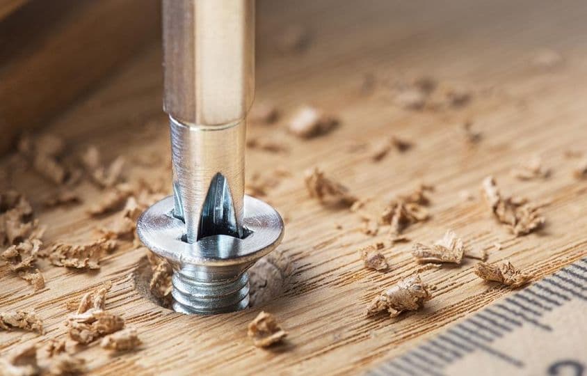 Csavarhúzóval csavart csavar egy tölgyfa deszkában.