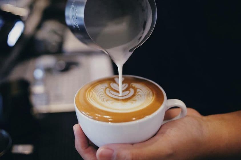 Barista tejet önt egy kávésbögrébe.