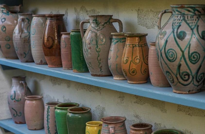 Kézzel festett kerámia kancsók és edények gyűjteménye kék fapolcokon.