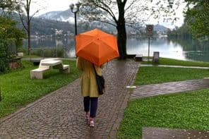 Nő sétál a tó mentén az esőben egy esernyővel.