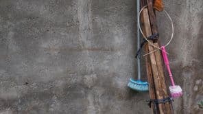 Rusztikus takarítóeszközök lógnak egy faoszlopon.