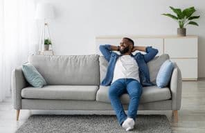 Férfi aki szakállas ül a kanapén.