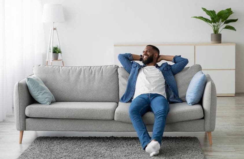 Férfi aki szakállas ül a kanapén.
